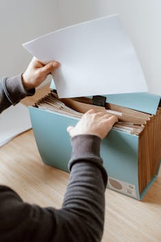 Crop anonymous male putting blank sheet of paper in case placed on wooden table